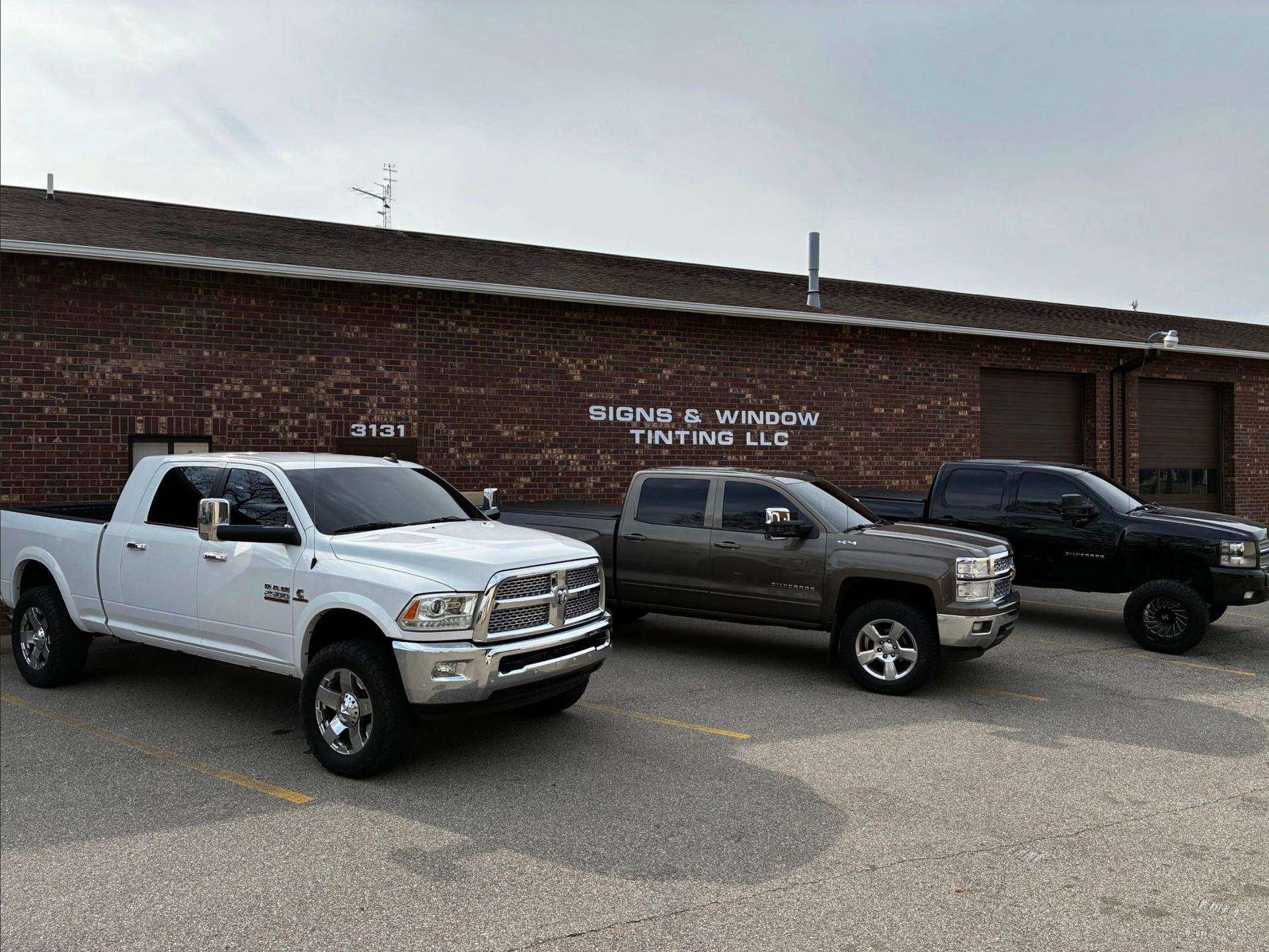 Three pickup trucks parked outside a brick building with white lettering.