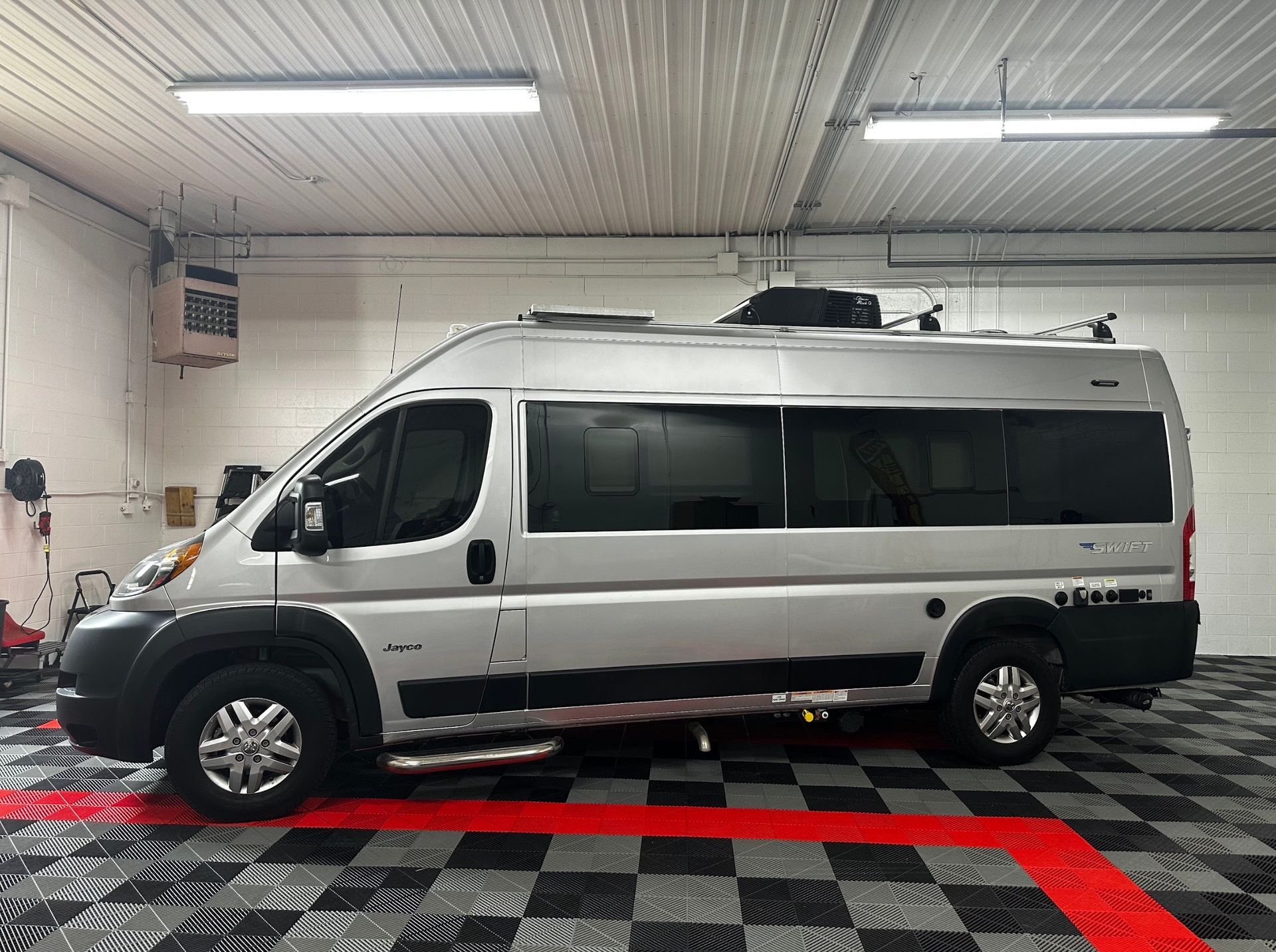 Silver passenger van parked indoors on a checkered floor under fluorescent lights