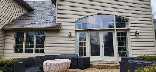 Back patio with sliding glass door, windows, and black wicker seating on a tan-sided house