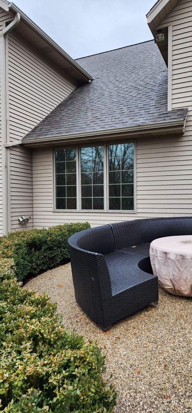 Front patio with black outdoor sofa and pink ottoman beside a beige house and window