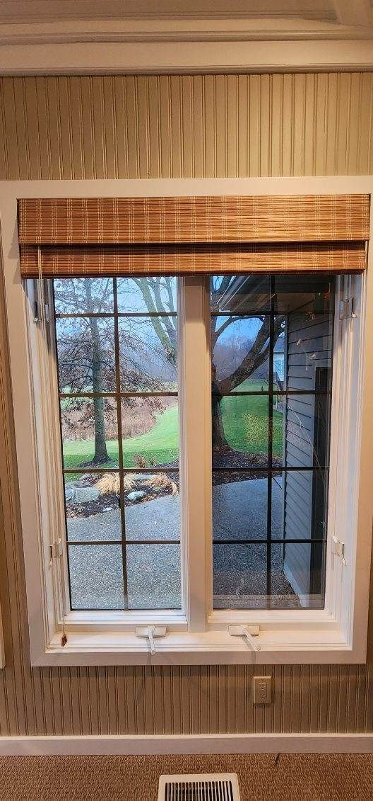Window with beige blinds and woven shades, looking out onto a backyard and stone path.