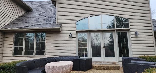 Back patio with curved glass doors, tan siding, and black outdoor seating on a stone patio