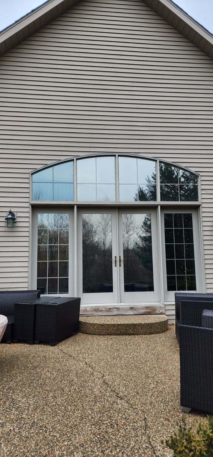 Suburban house exterior with large arched windows, gravel patio, and black outdoor chairs