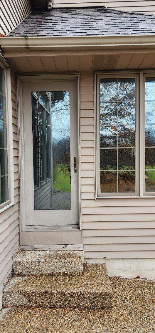 Front entrance with glass storm door, narrow steps, and beige siding on a house