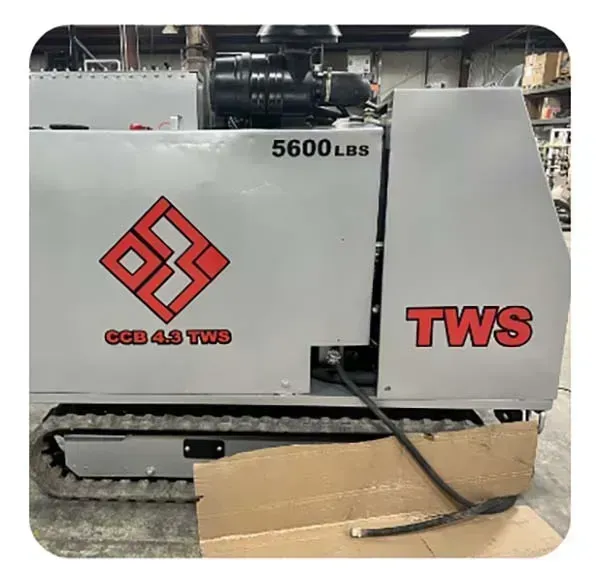 Gray TWS industrial machine with red logos in a workshop, cardboard and a hose on the floor