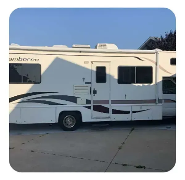 White and gray motorhome parked on a concrete lot under a clear blue sky.