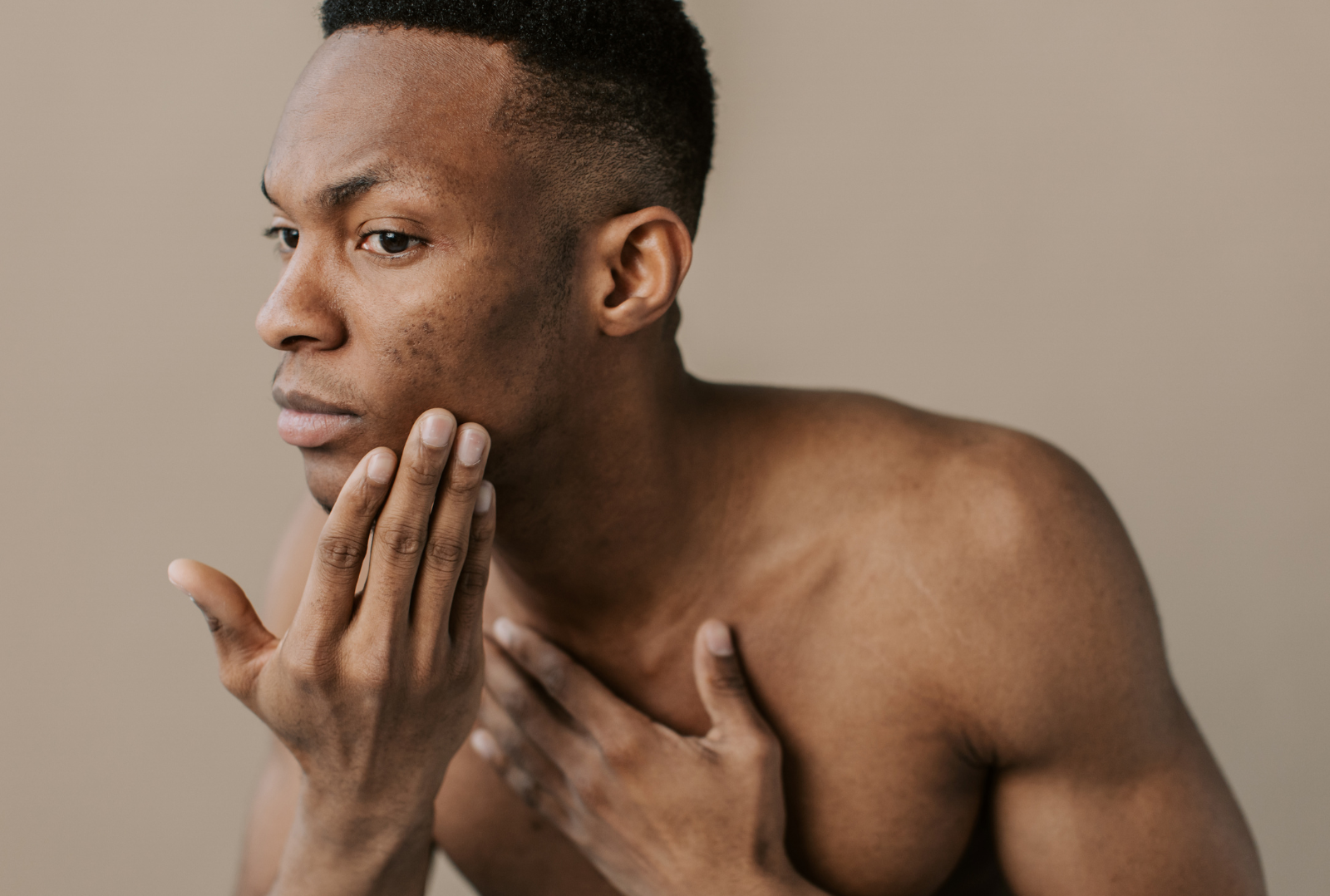 Man touches face, examining skin. Beige background.