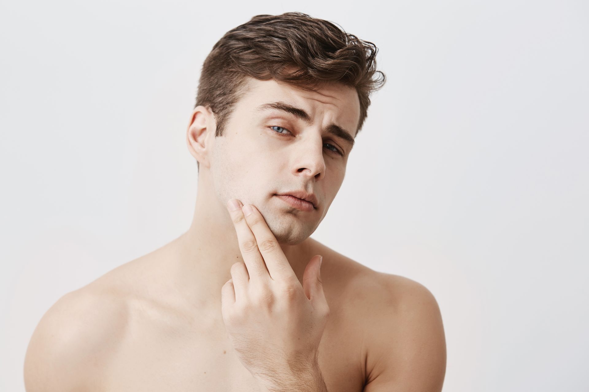 Man touching his cheek, looking concerned, against a white backdrop.