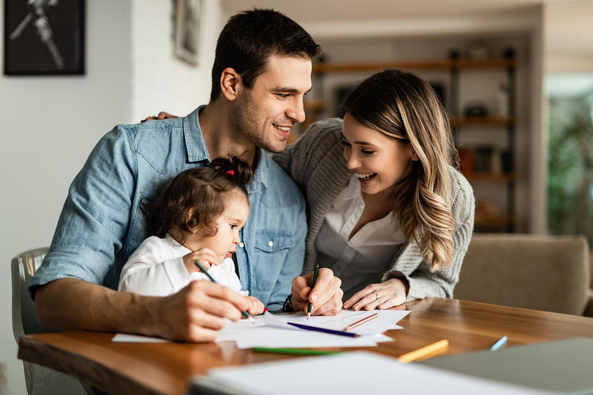 Family sitting at a table, smiling and writing in a notebook together in a bright living room