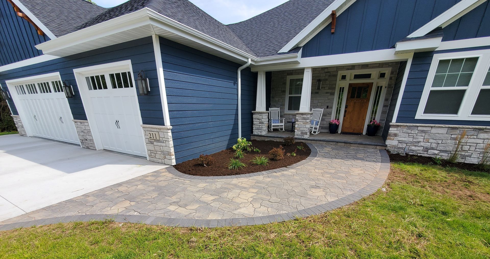 A blue house with a new brick walkway leading to the front door with some newly planted bushes and fresh mulch in Wausau, Wisconsin.