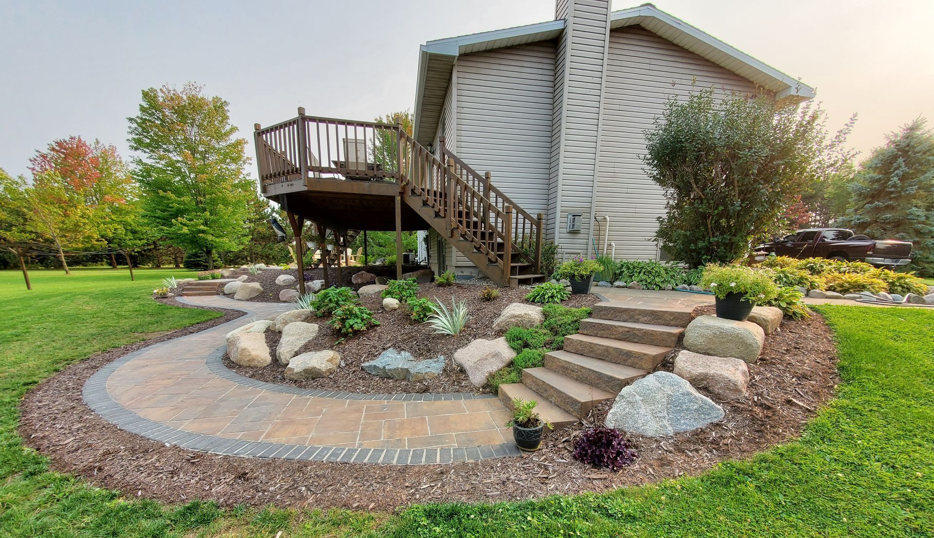 A house with a deck and stairs in the backyard with newly installed brick walkway, stone staircase and new landscaping in Wausau, Wisconsin