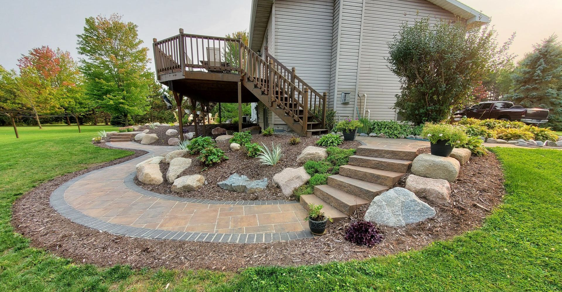 A house with a deck and stairs in the backyard with newly installed brick walkway, stone staircase and new landscaping in Wausau, Wisconsin