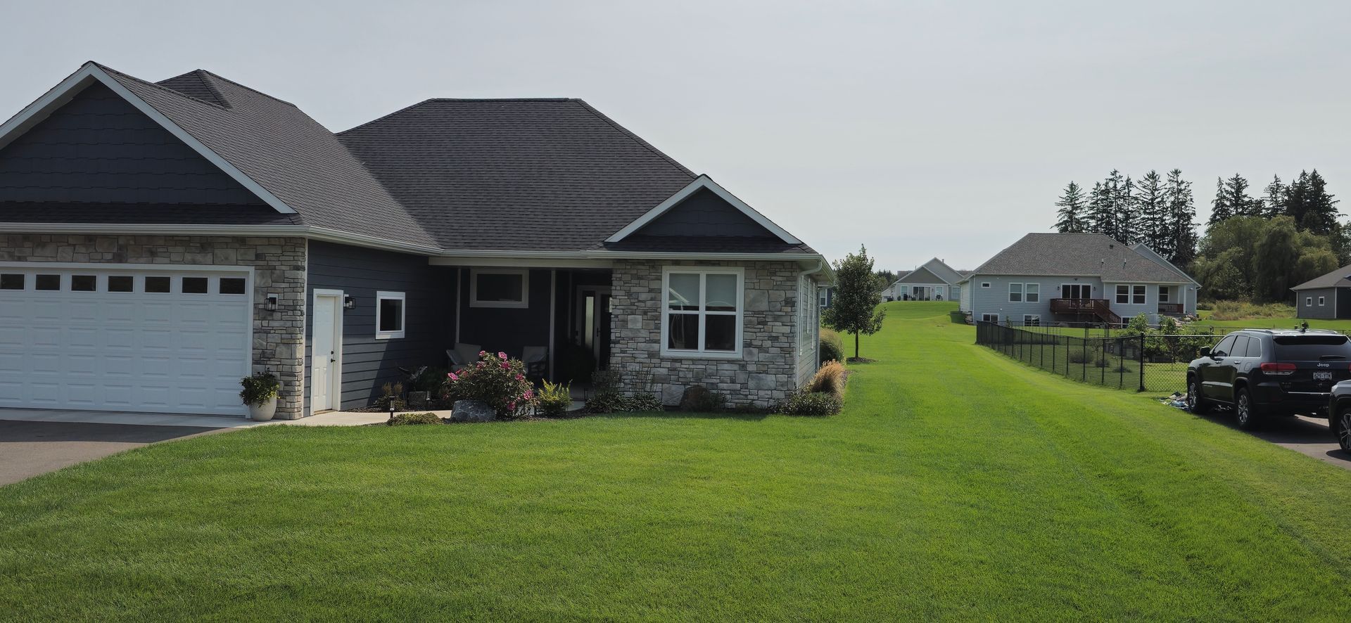 A house with a white garage door is sitting on top of a lush green hillside.