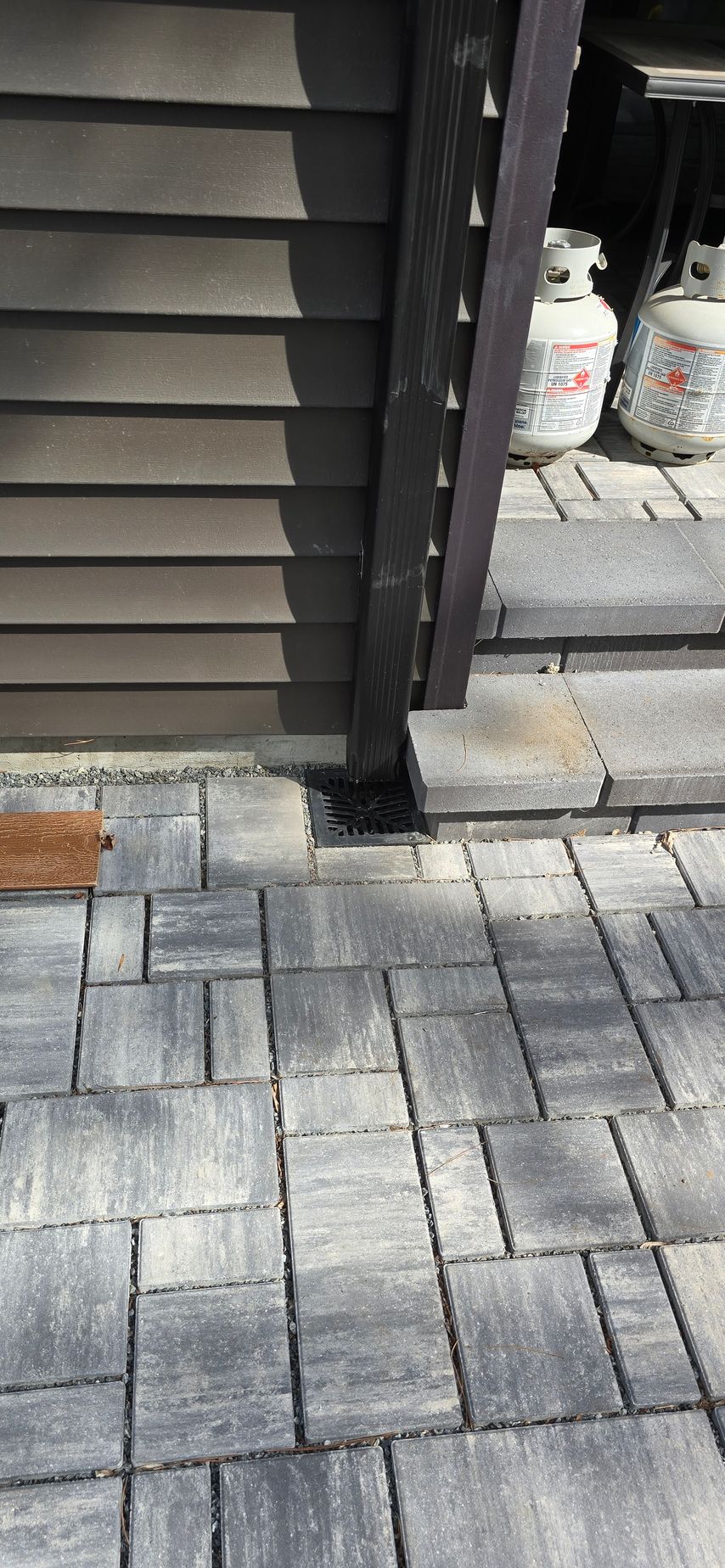 A brick walkway next to a house with a gutter drain in the background.