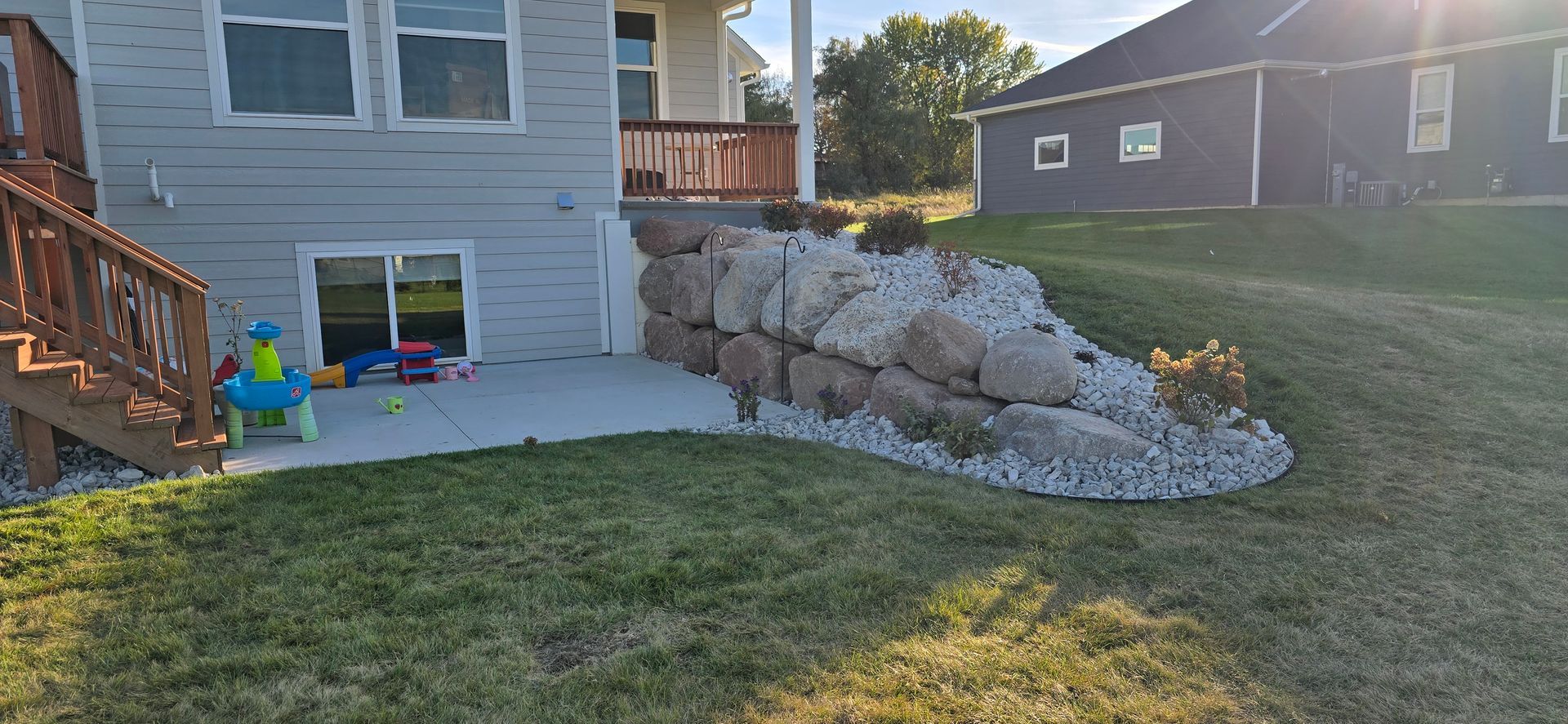 The backyard of a house with a newly installed plant bed with river rock and plants with plastic edging in Rothschild, Wisconsin