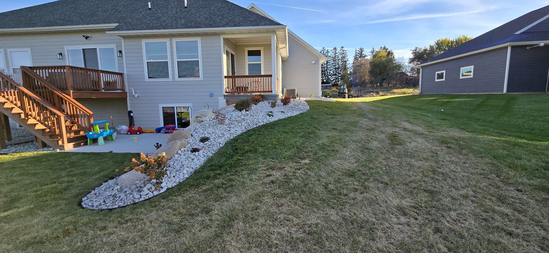 The backyard of a house with a newly installed plant bed with river rock and plants with plastic edging in Rothschild, Wisconsin