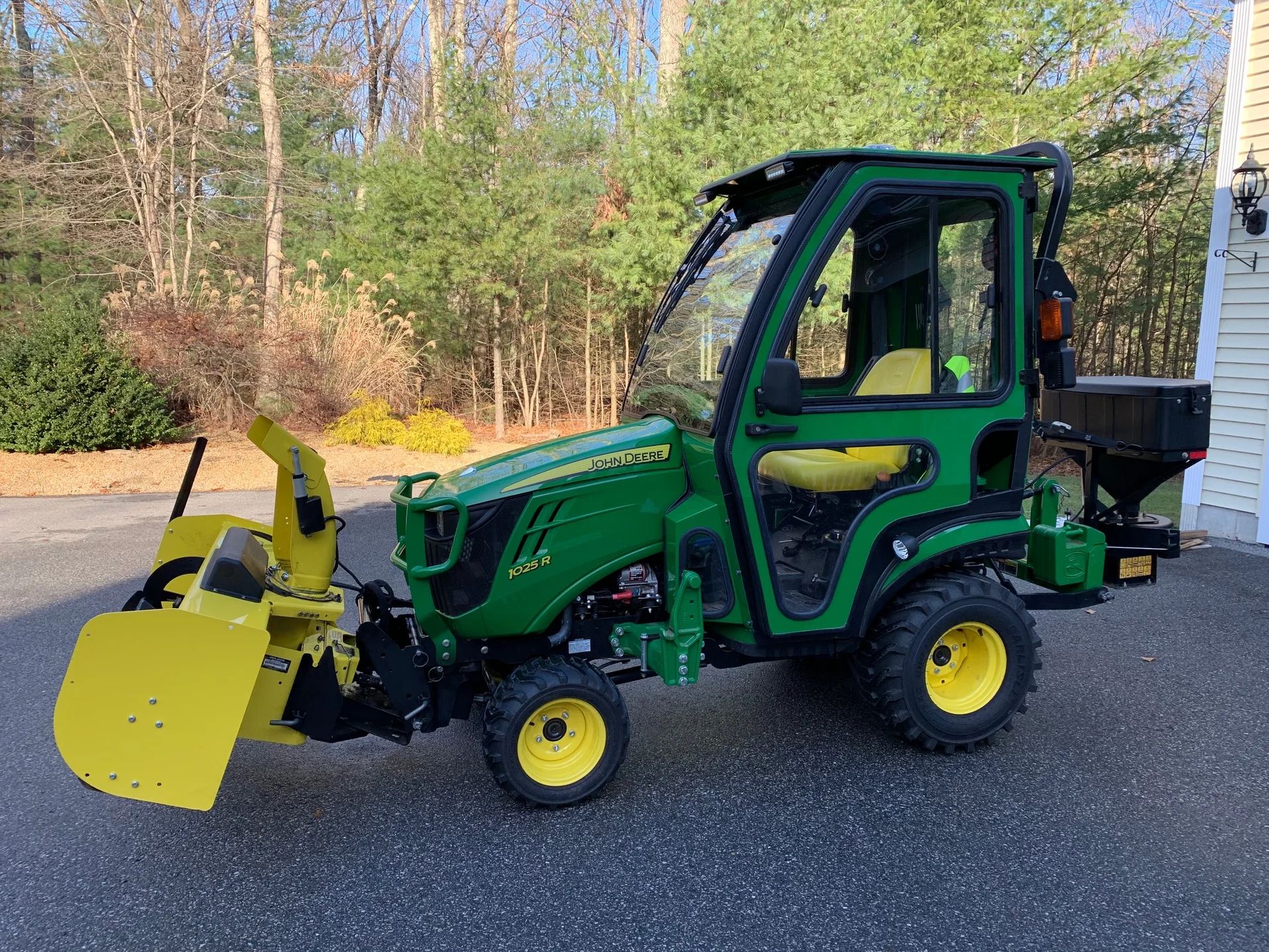 Green John Deere tractor with a snowblower, parked outdoors on a paved surface.