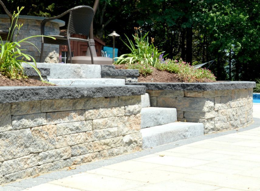 A newly installed stone wall with new stone stairs leading up to a patio next to a pool in Wausau, Wisconsin