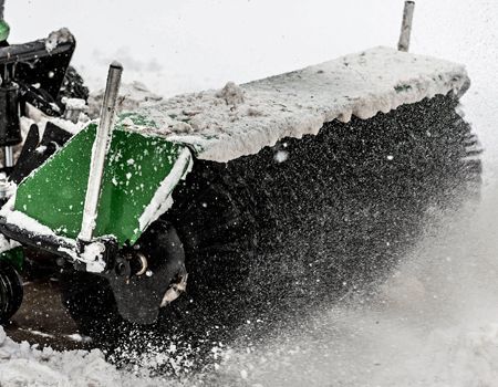 Snow-covered brush of a green and black snow sweeper in action, clearing snow in Mosinee, Wisconsin.