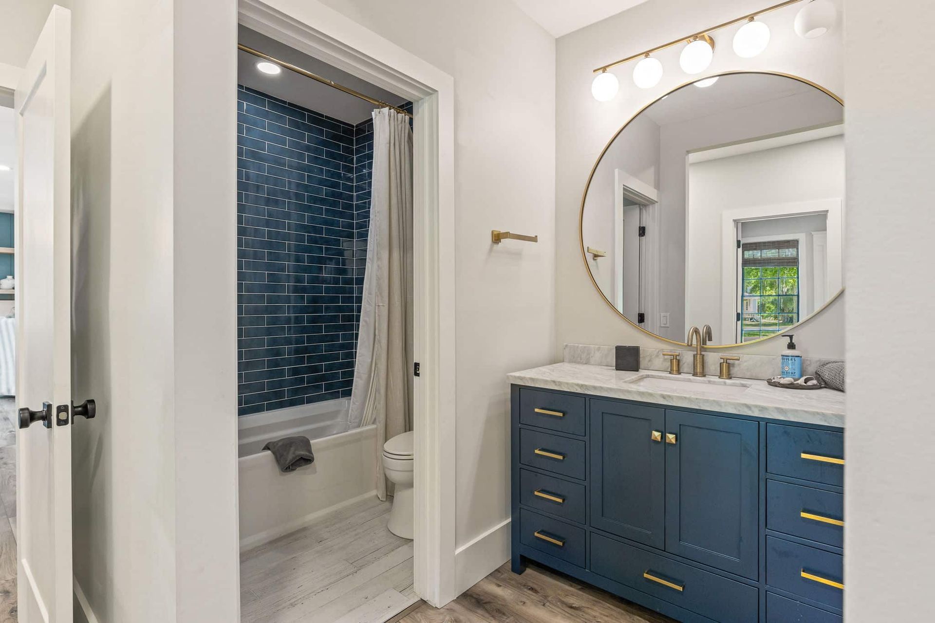 A bathroom with blue cabinets , a toilet , and a large mirror.