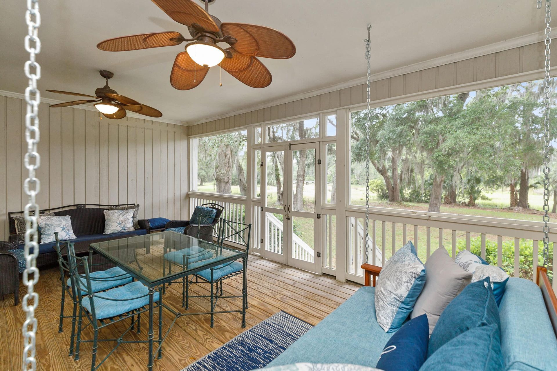 A screened in porch with a couch , table , chairs and ceiling fans.