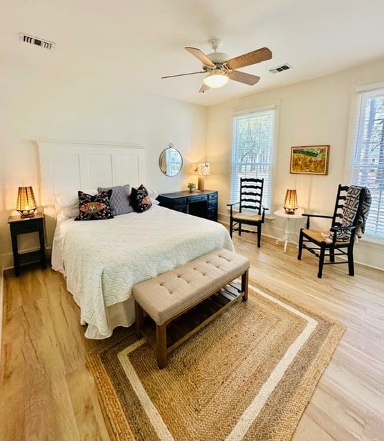 A bedroom with a bed , chairs , a bench and a ceiling fan.