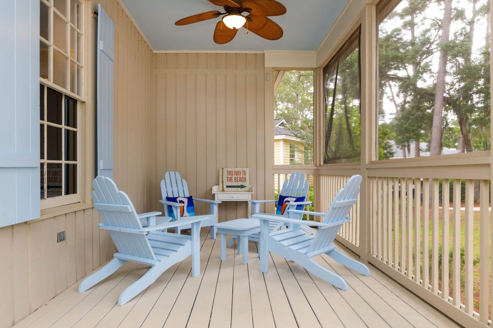 A screened in porch with blue chairs and a ceiling fan
