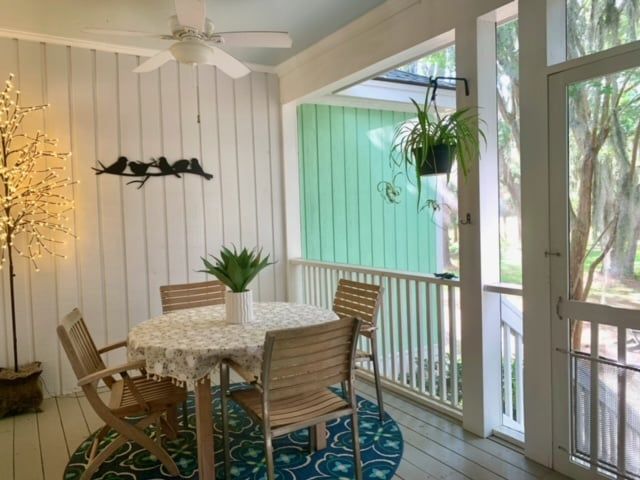A screened in porch with a table and chairs and a ceiling fan