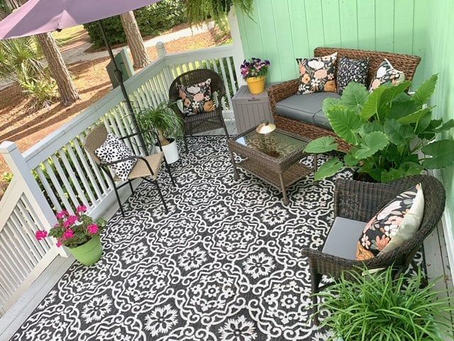 A porch with a couch , chairs , table and umbrella.