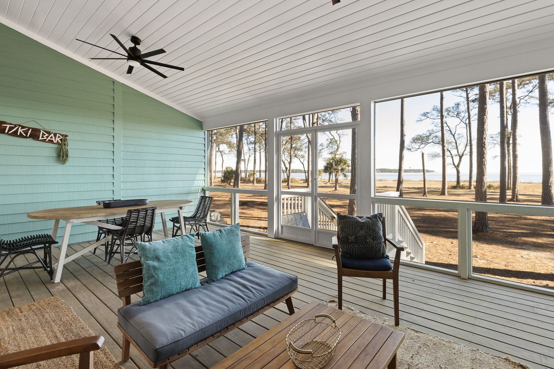 A screened in porch with a couch , chairs , table and ceiling fan.