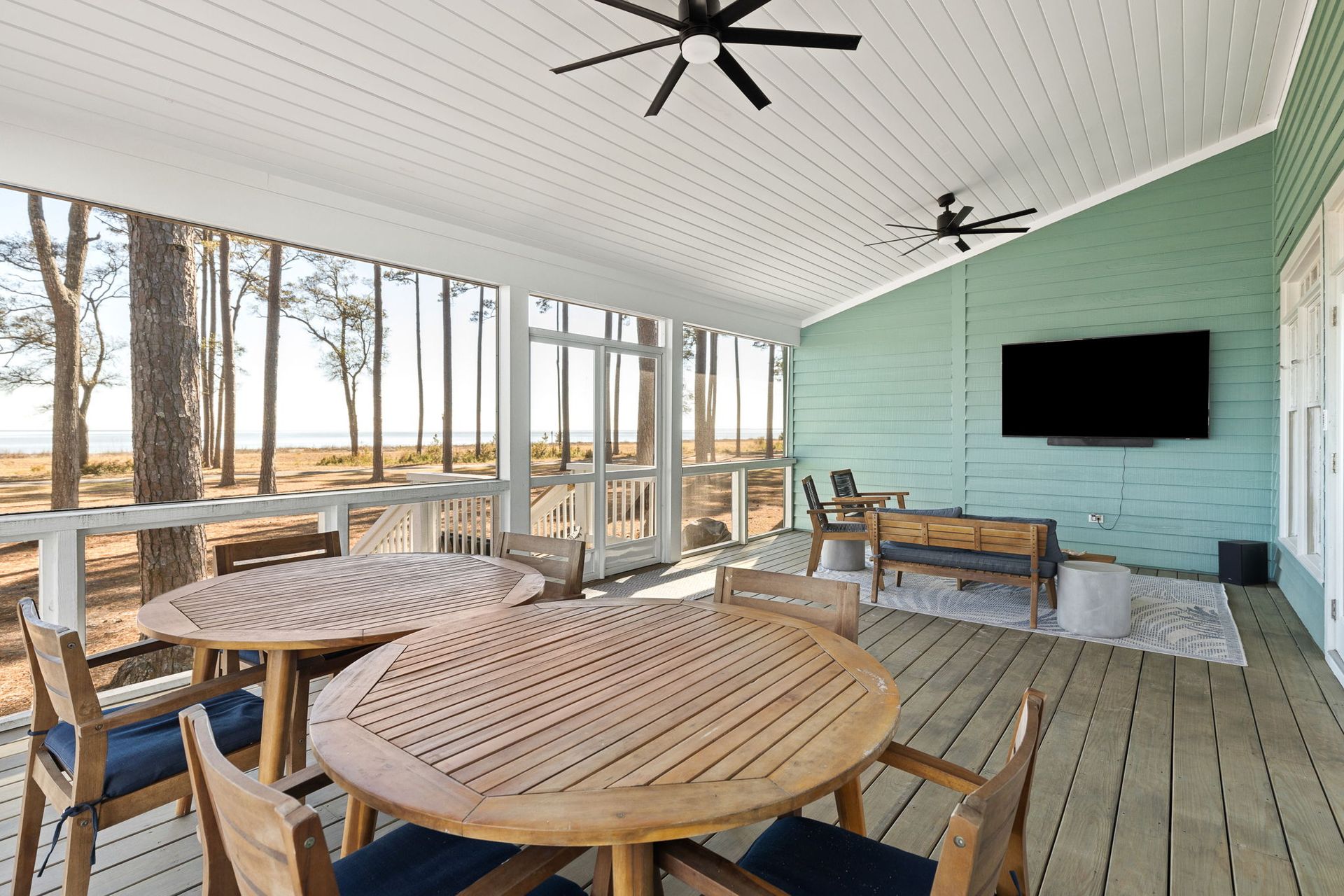 A screened in porch with tables and chairs and a flat screen tv.
