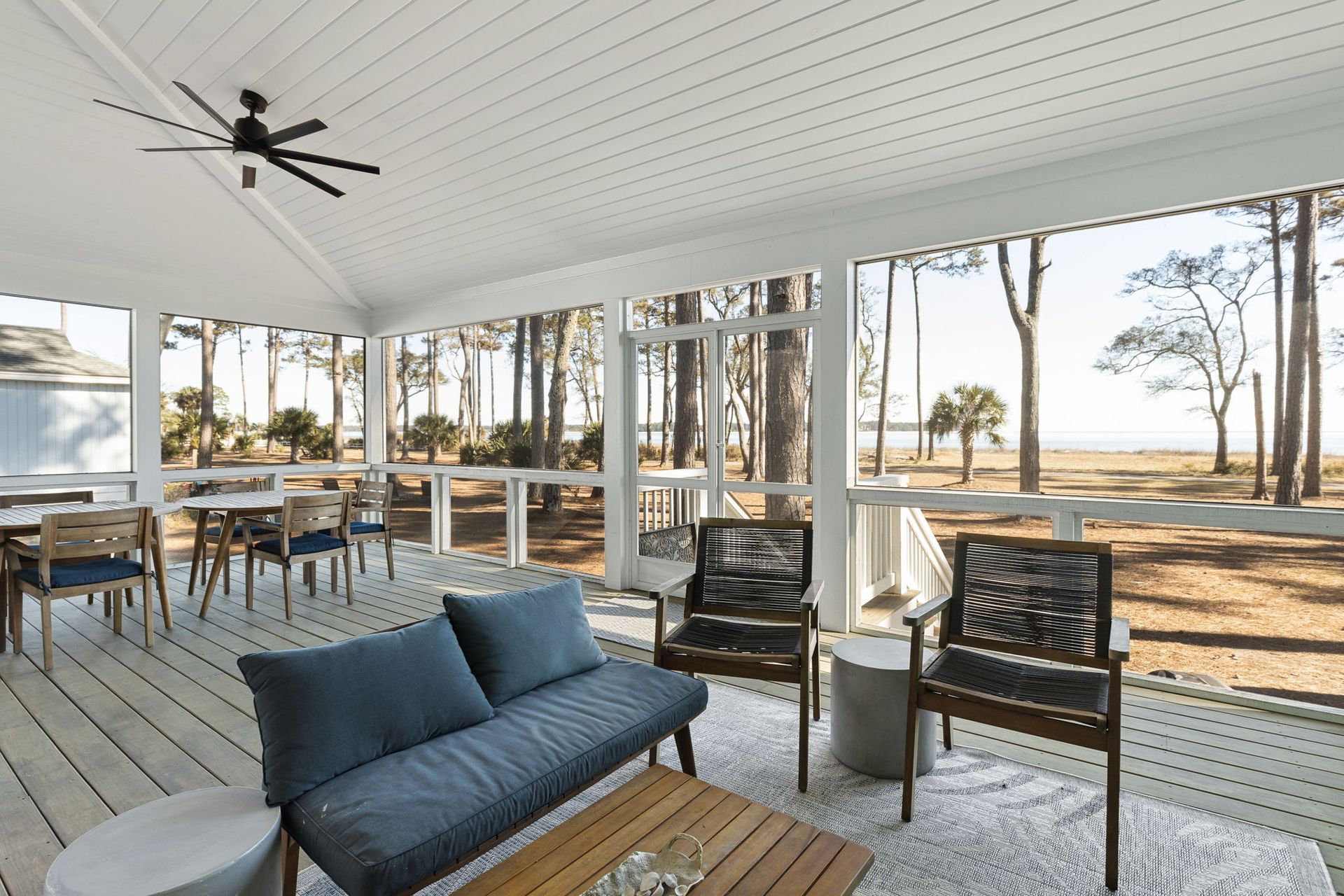 A screened in porch with a couch , chairs , table and ceiling fan.