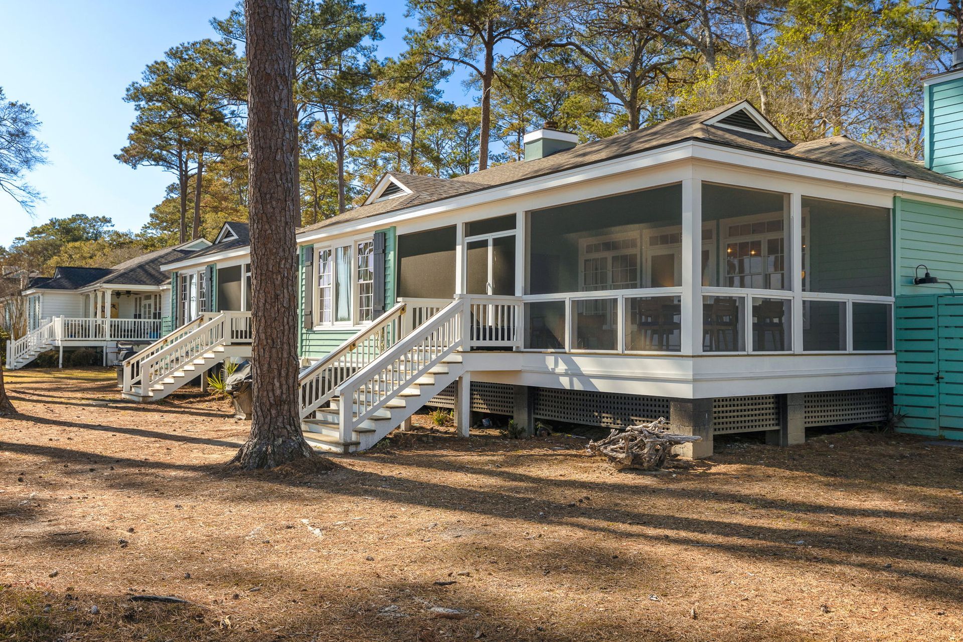 A small house with a screened in porch is surrounded by trees.