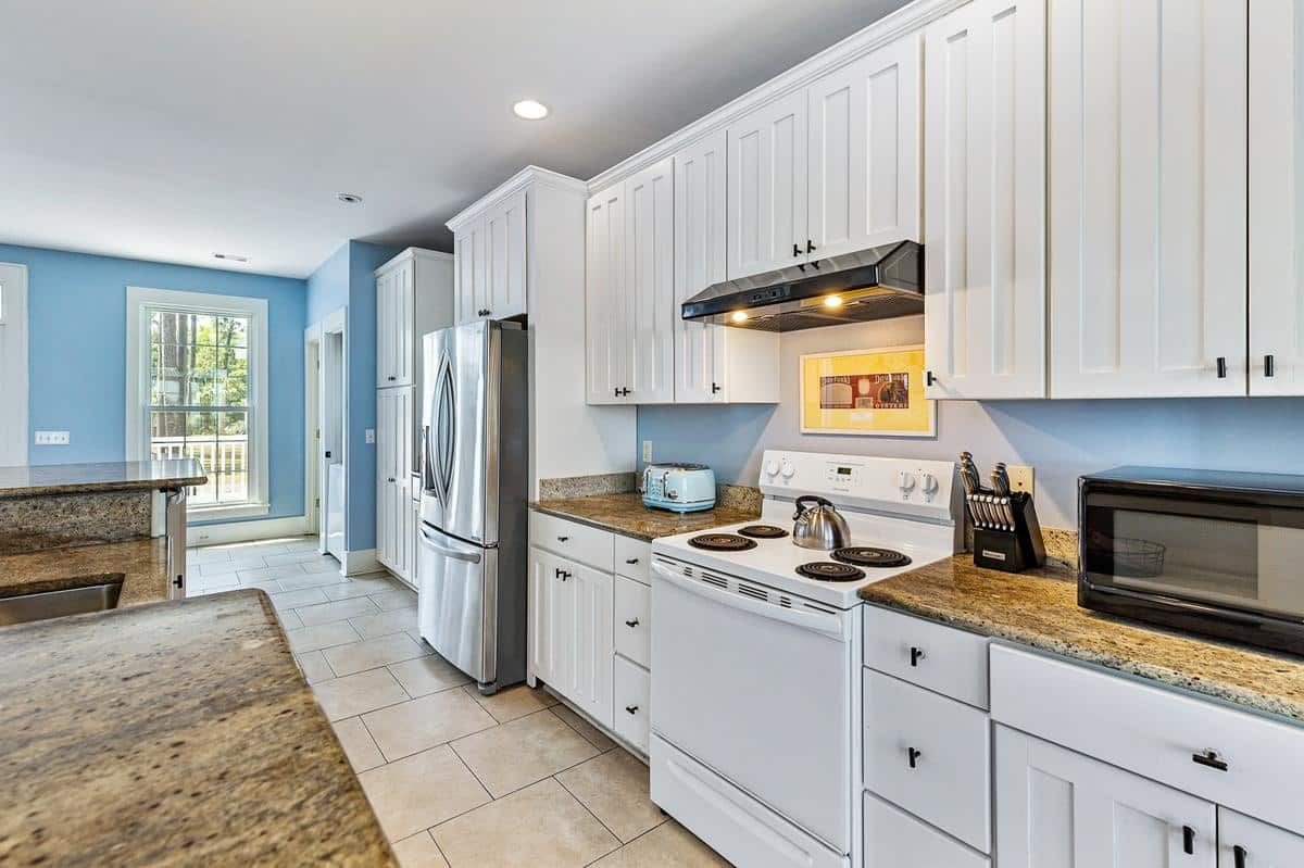 A kitchen with white cabinets , granite counter tops , a stove , refrigerator and microwave.