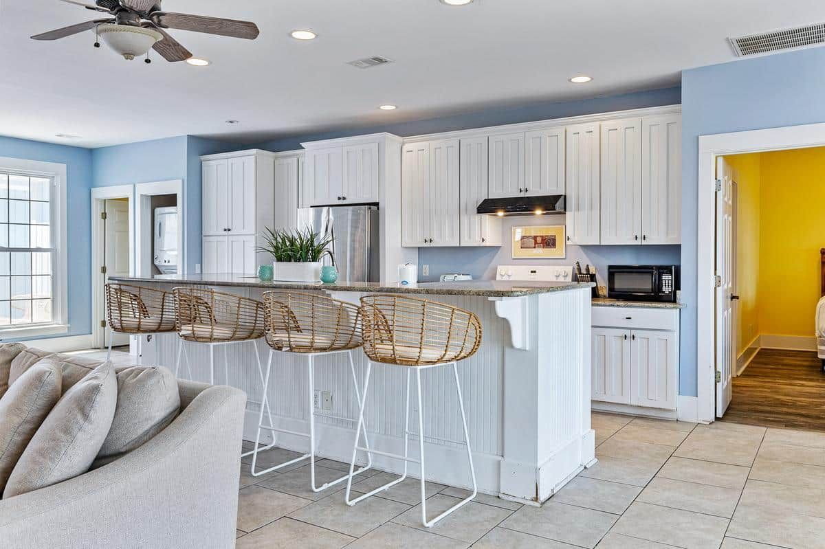A kitchen with white cabinets and stools and a ceiling fan.