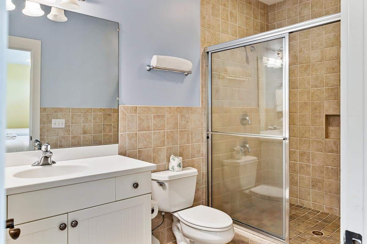 A bathroom with a toilet , sink , mirror and walk in shower.