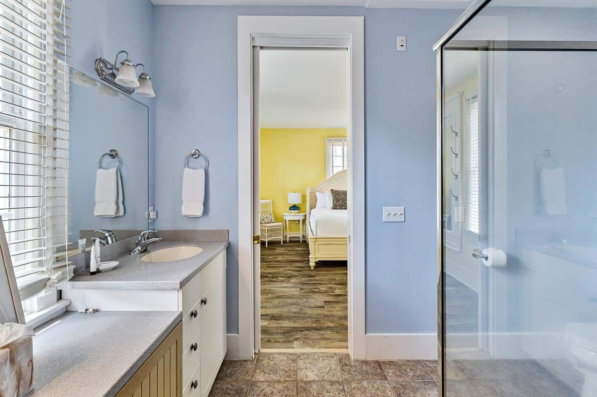A bathroom with blue walls and a walk in shower leading to a bedroom.