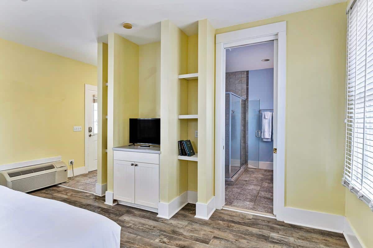 A bedroom with a bed , television , shelves and a door leading to a bathroom.