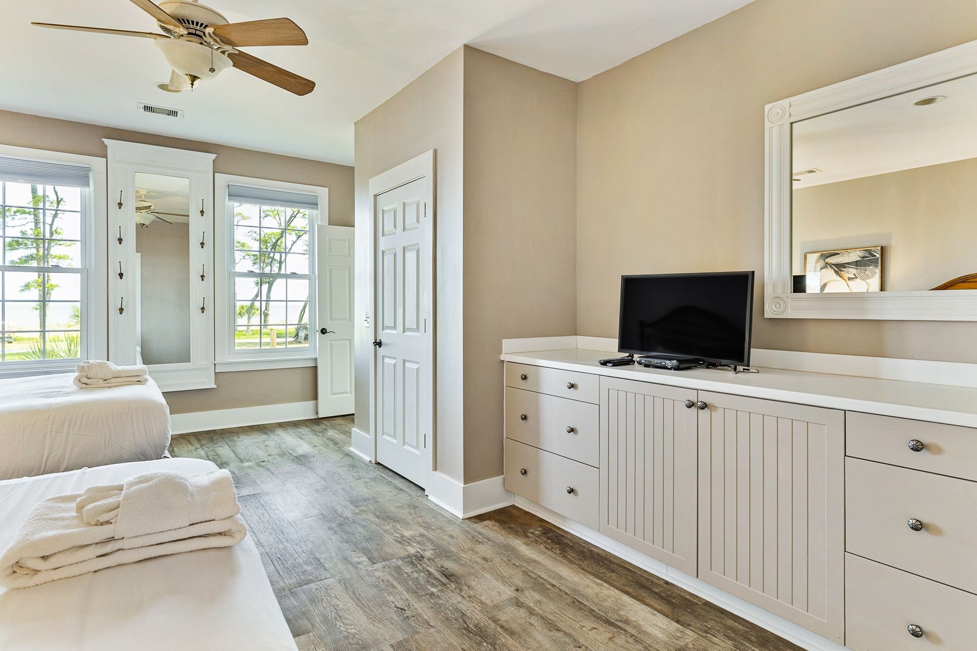 A bedroom with two beds , a television , a mirror and a ceiling fan.