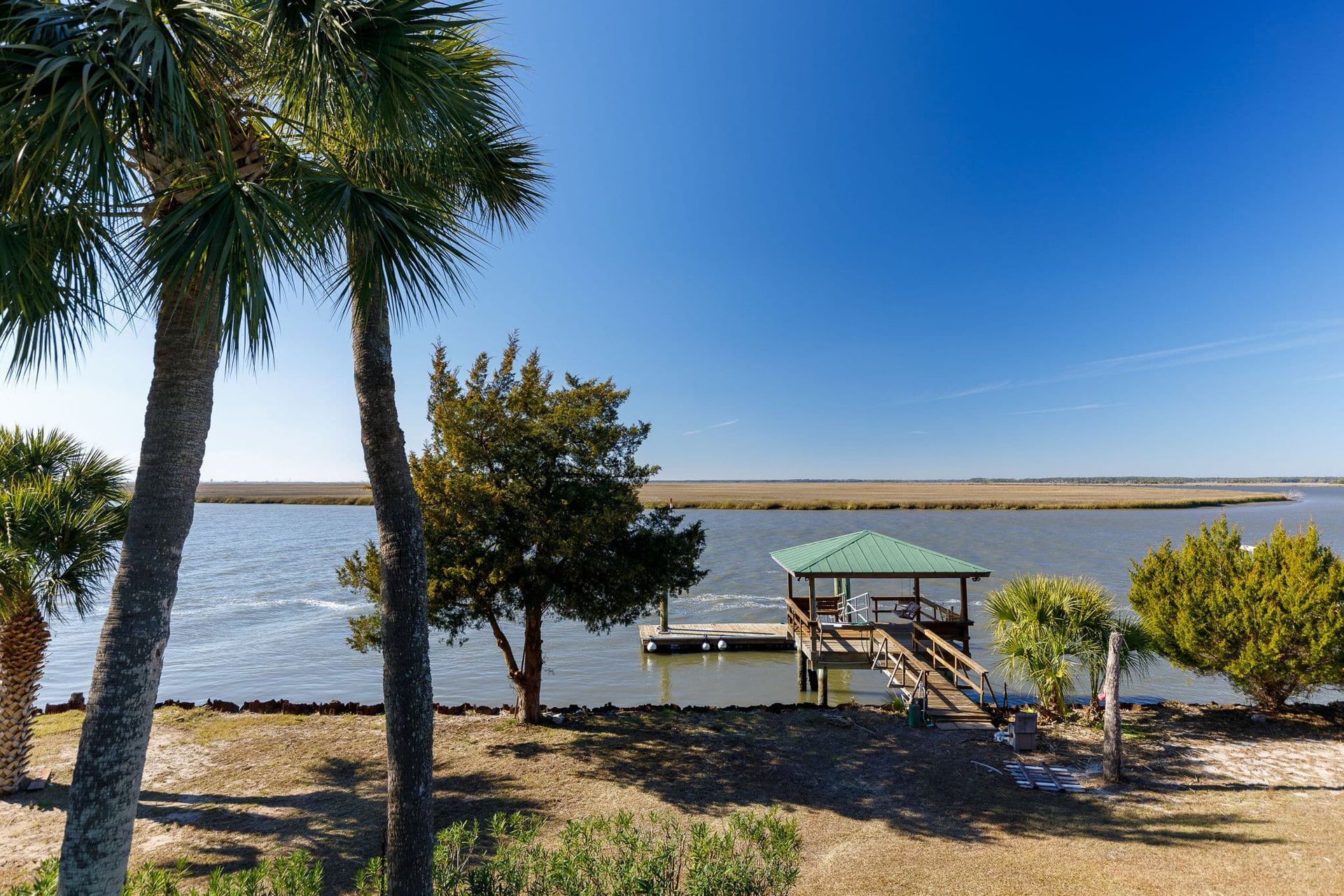 A dock with a green roof is surrounded by palm trees and a body of water.