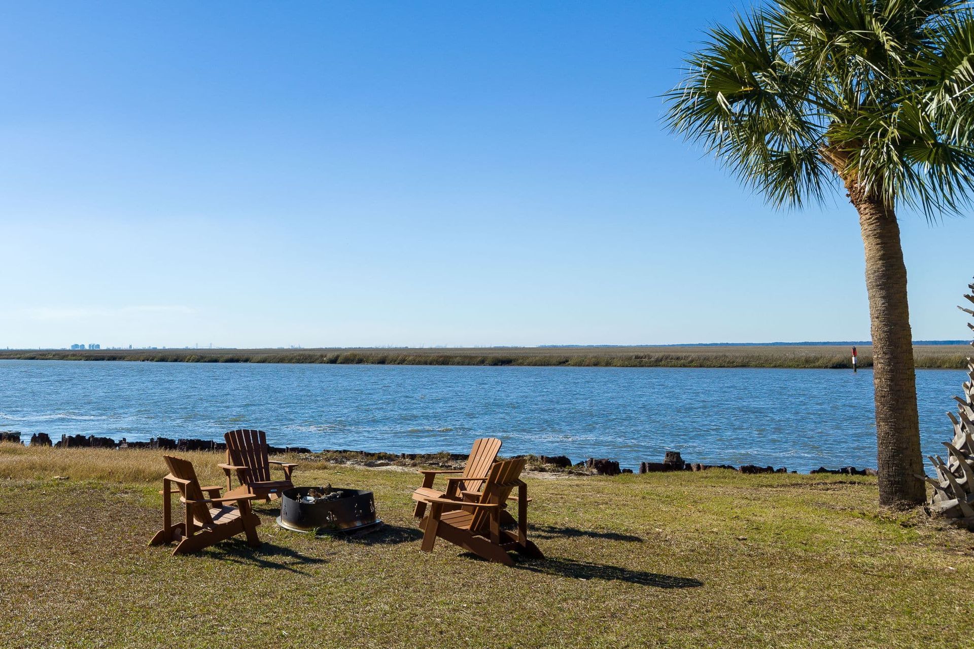 A group of chairs are sitting next to a fire pit on the shore of a lake.
