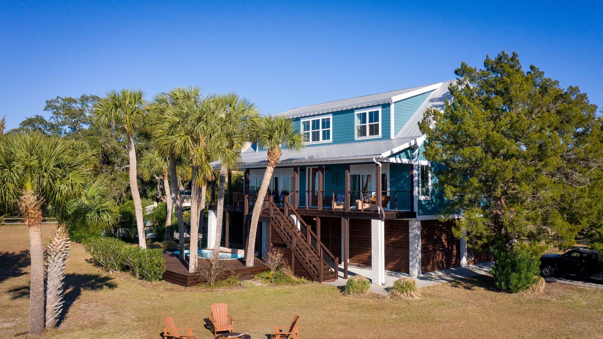 An aerial view of a large blue house surrounded by trees and chairs.