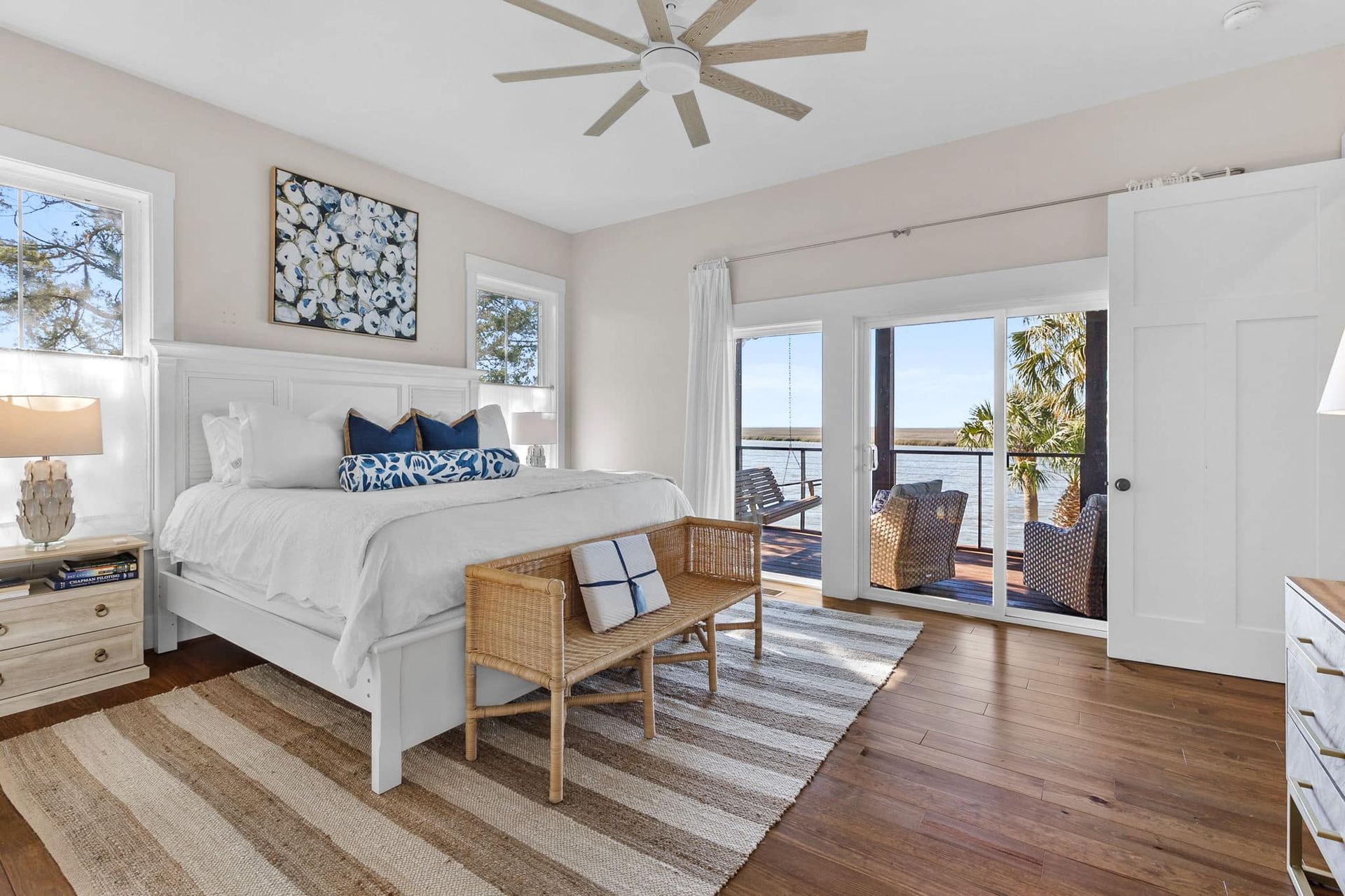 A bedroom with a large bed , sliding glass doors , a bench and a ceiling fan.