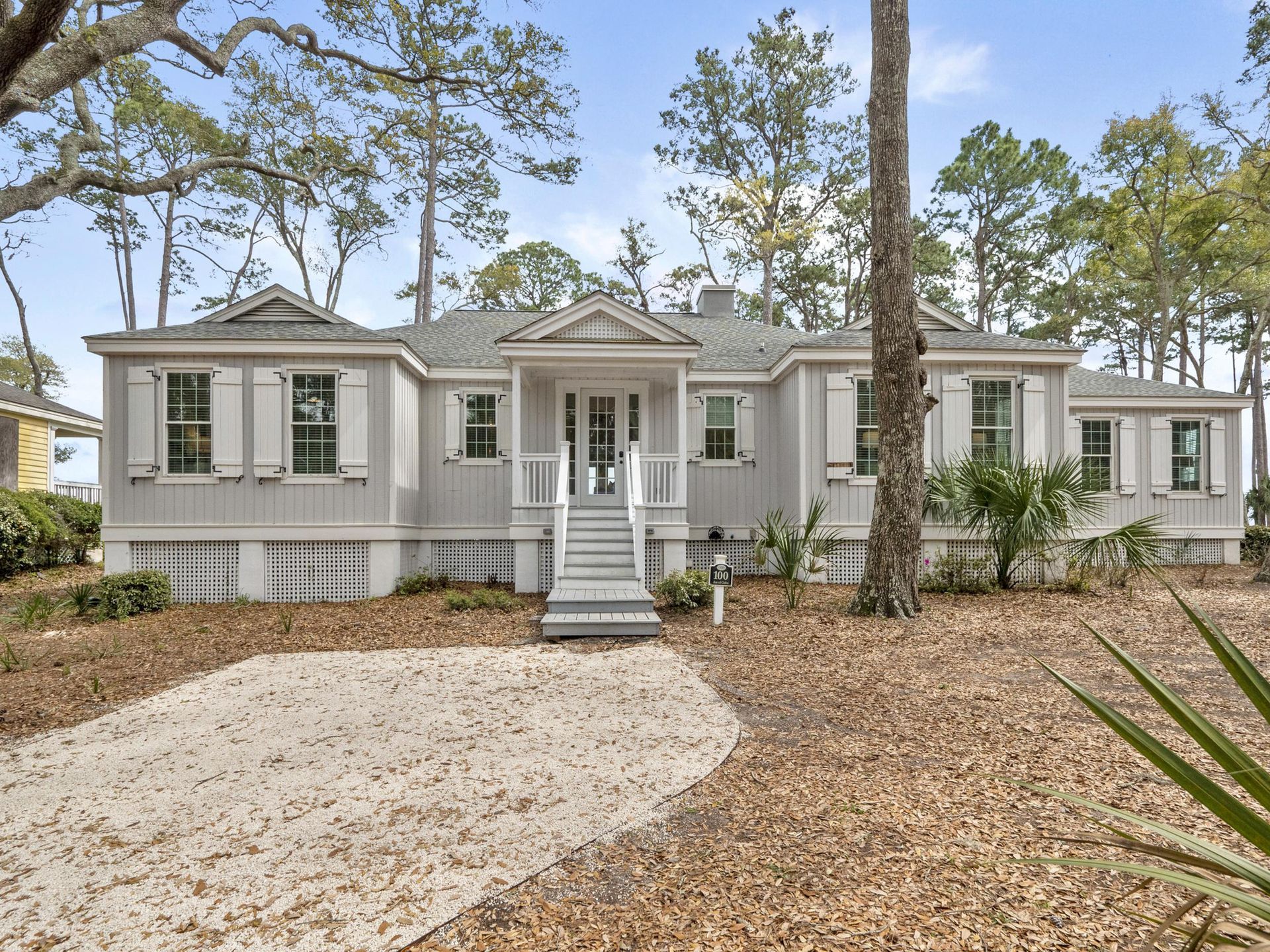 The front of a house with a driveway and trees in the background.