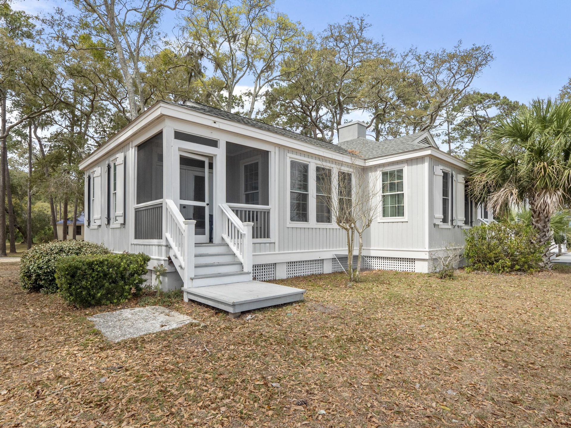 A small white house with a screened in porch surrounded by trees.