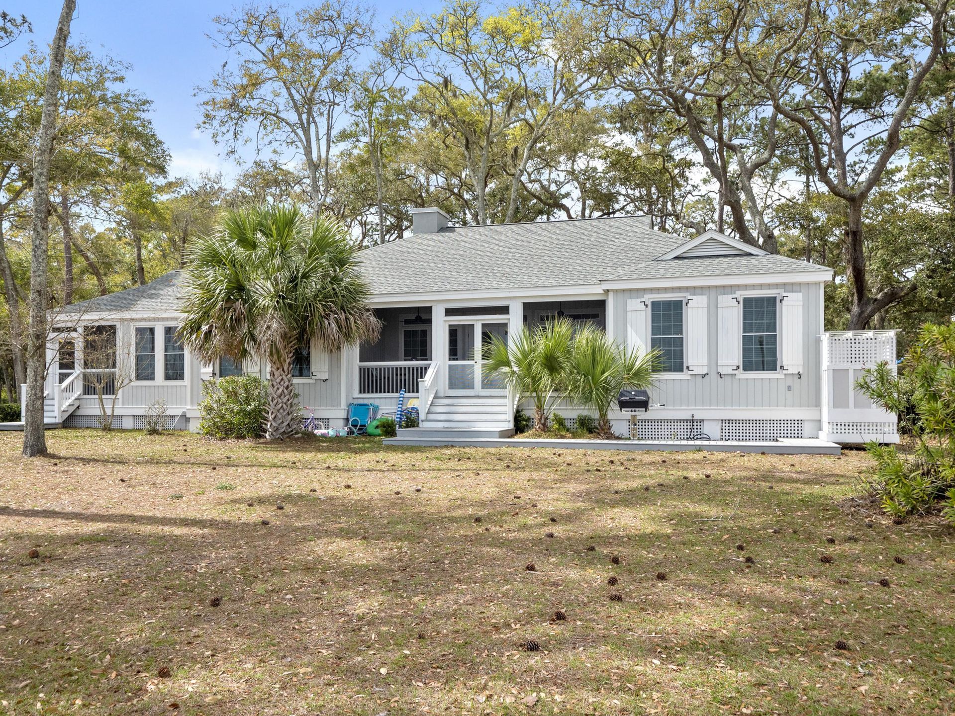 A white house with a screened in porch is surrounded by trees and grass.