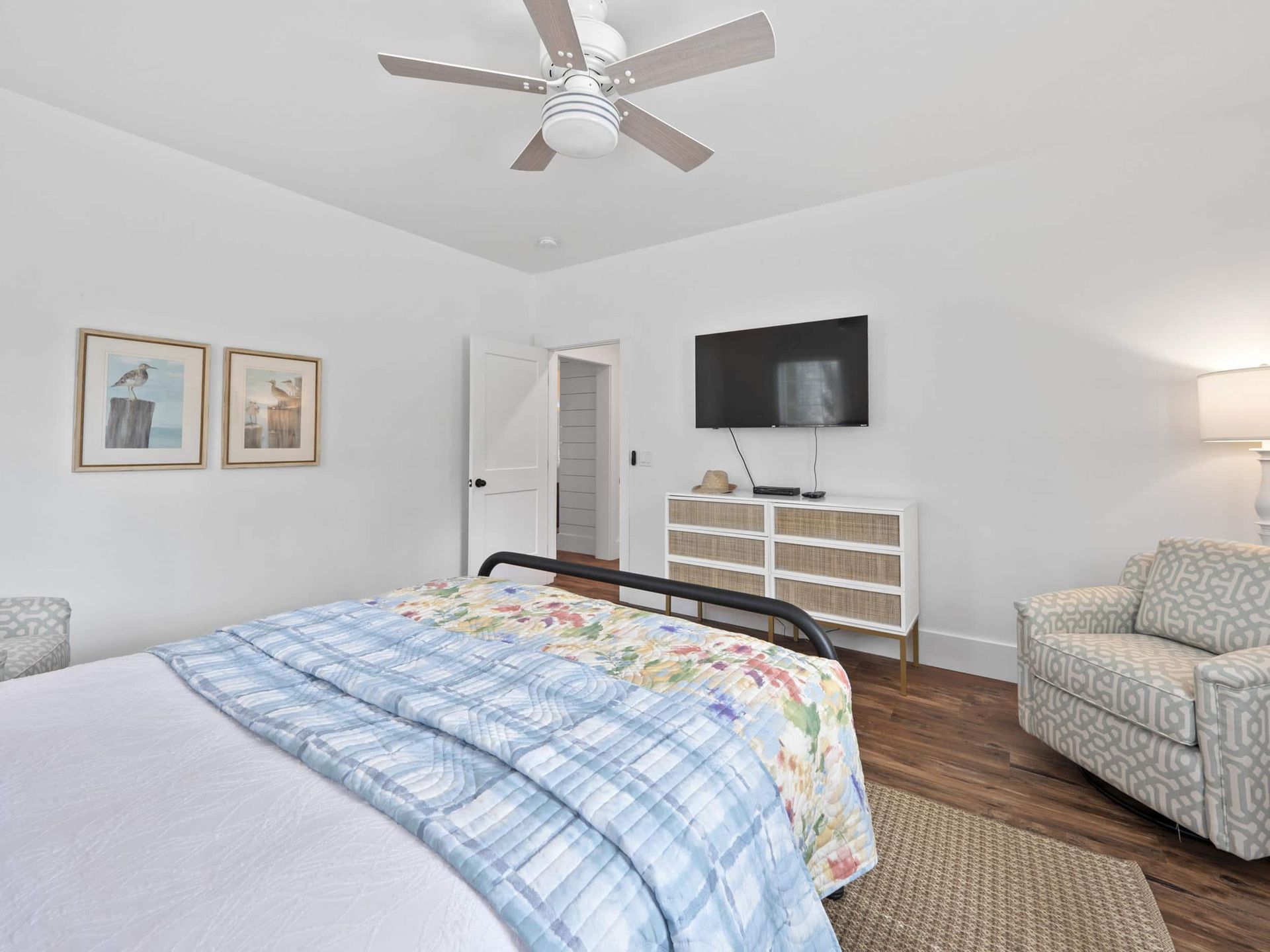 A bedroom with a bed , chair , dresser , television and ceiling fan.