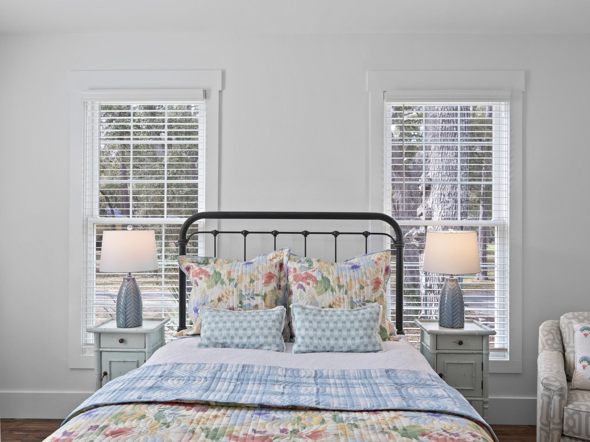 A bedroom with a bed , two nightstands , two lamps and two windows.