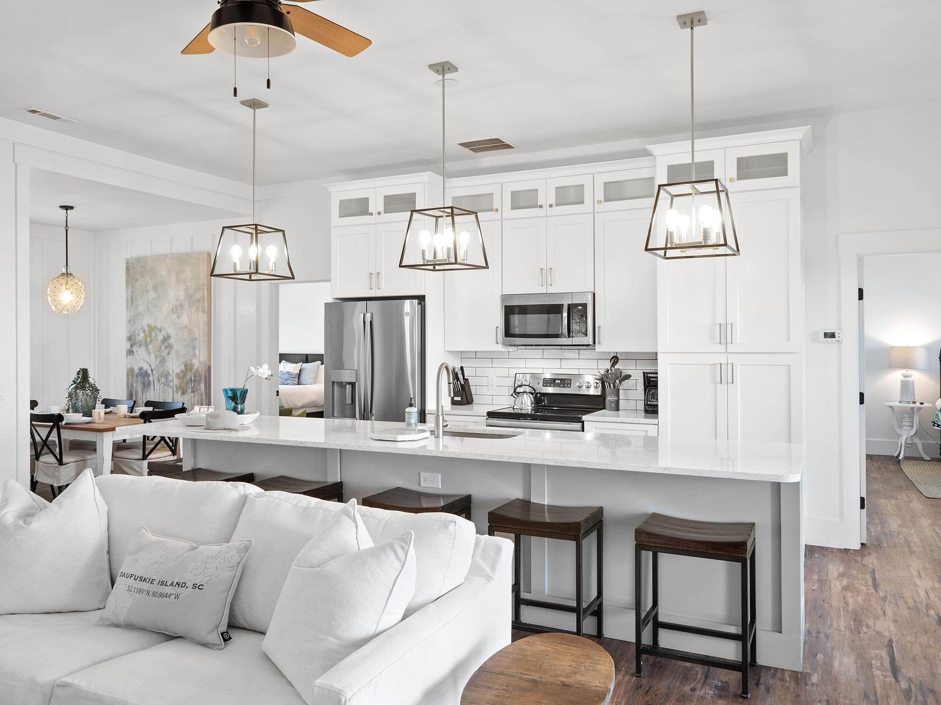 A living room with a couch , stools , a ceiling fan and a kitchen.