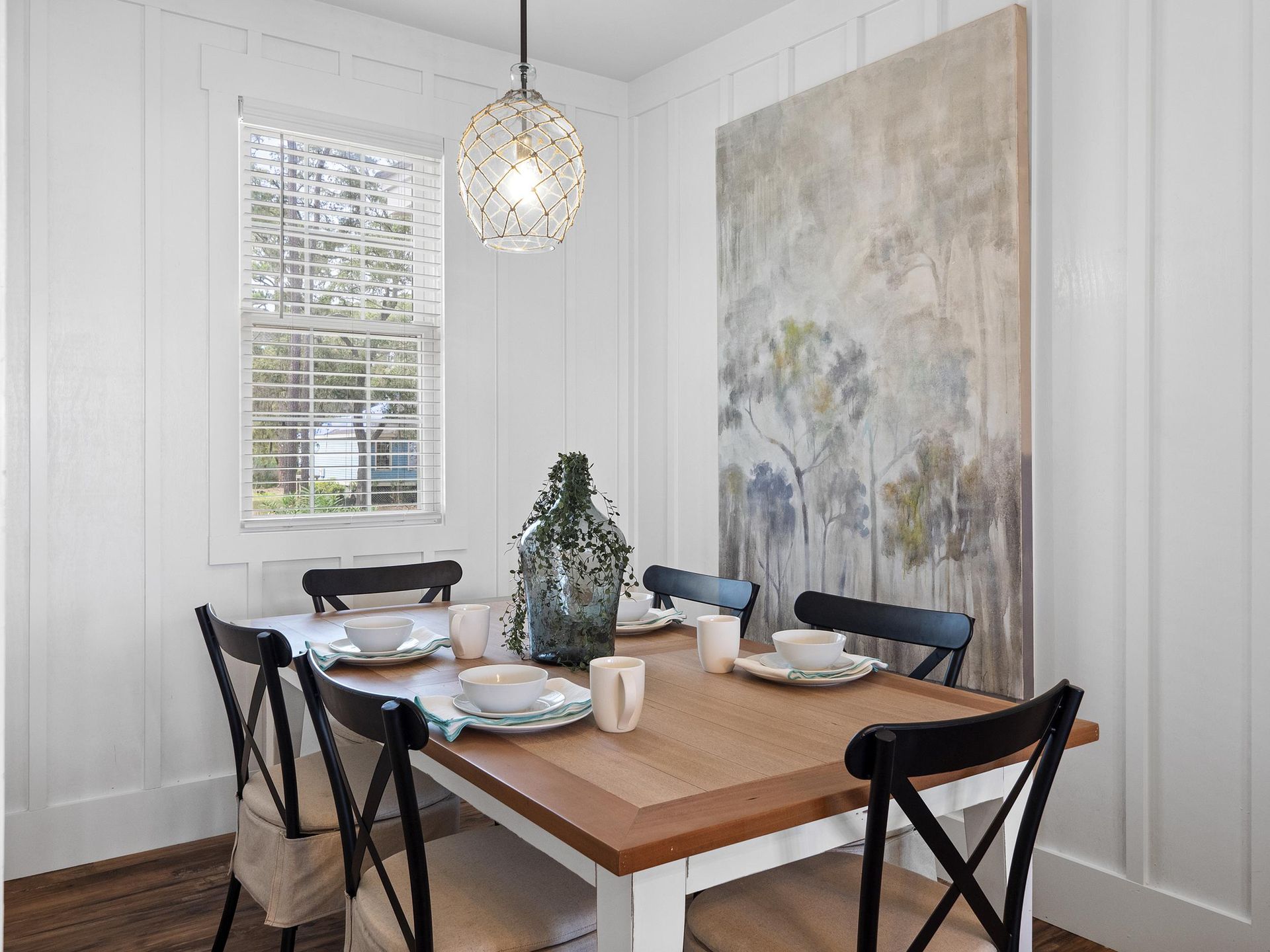 A dining room with a table and chairs and a painting on the wall.
